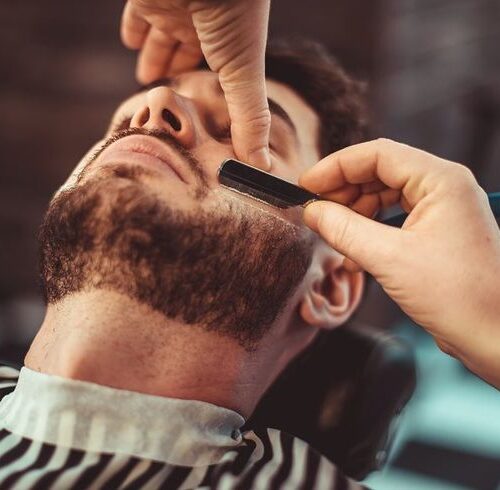 Barber shaving a bearded man in a barber shop, close-up